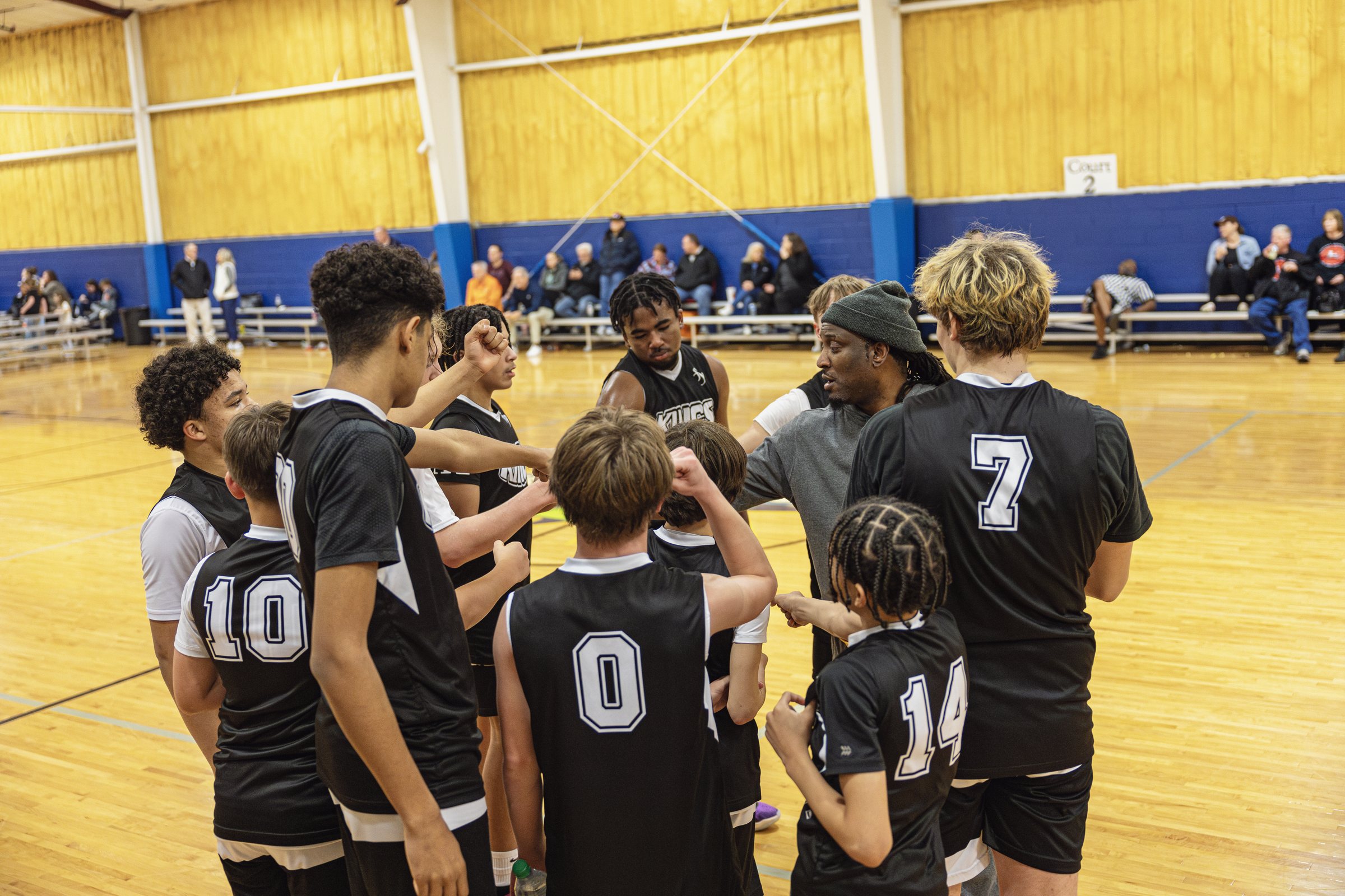 Kings Youth Basketball team huddled together with their coach on the court after a game.
